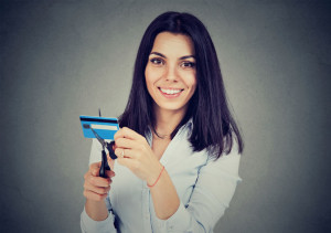 Happy woman cutting in half her credit card with scissors isolated on gray background